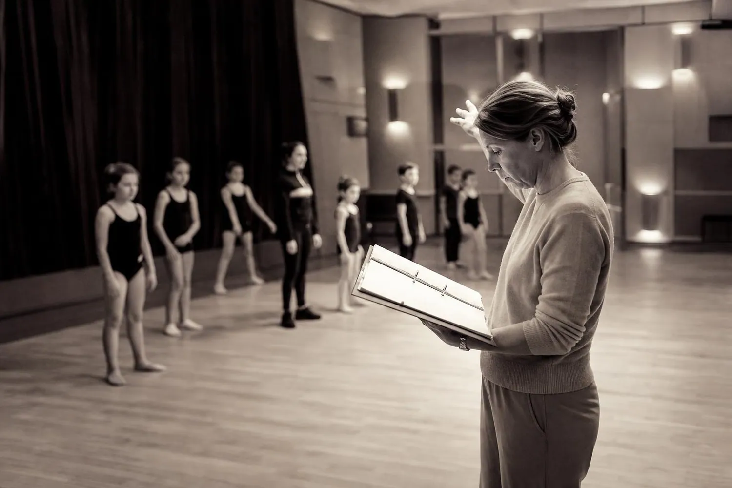 Directrice d’école de danse debout au bord du plateau d’une salle de spectacle, un classeur ouvert dans les bras, pendant l’installation avant la représentation